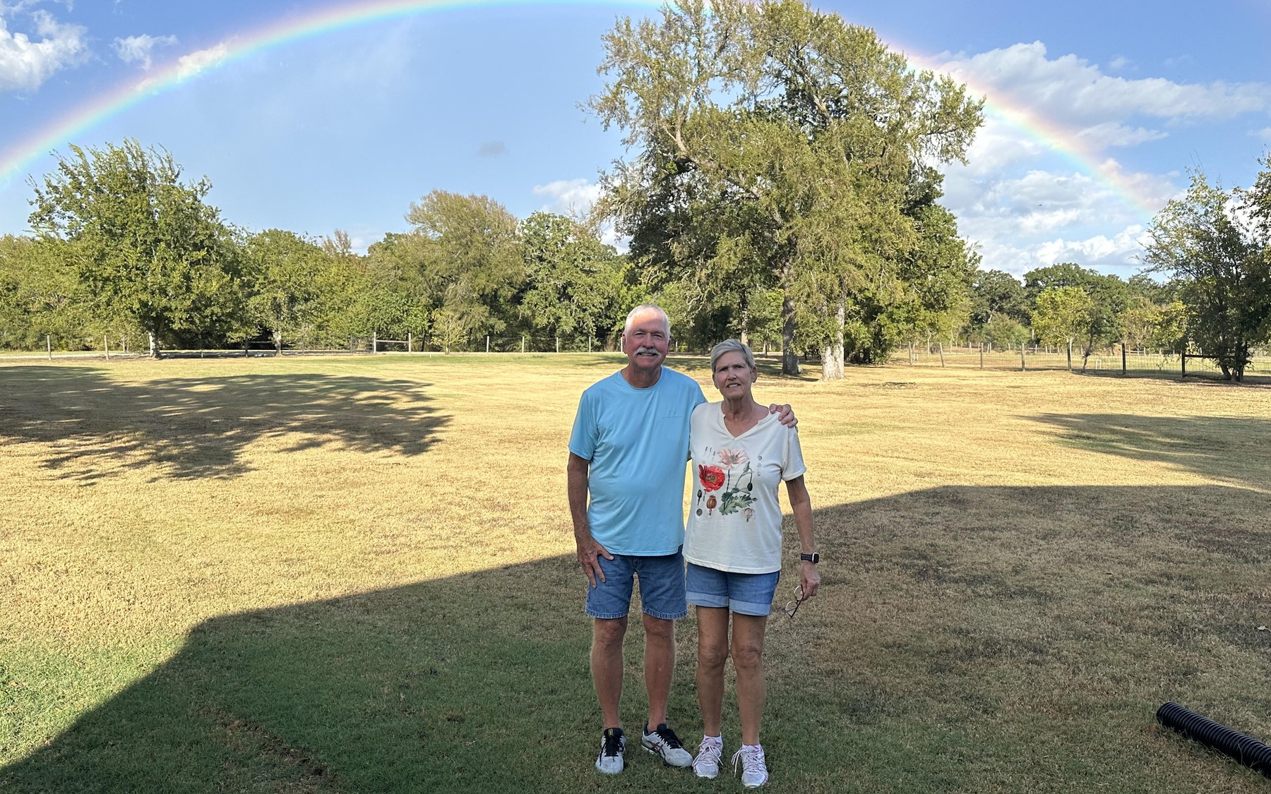 Amy and her husband Pat standing under a double rainbow on their Navasota property